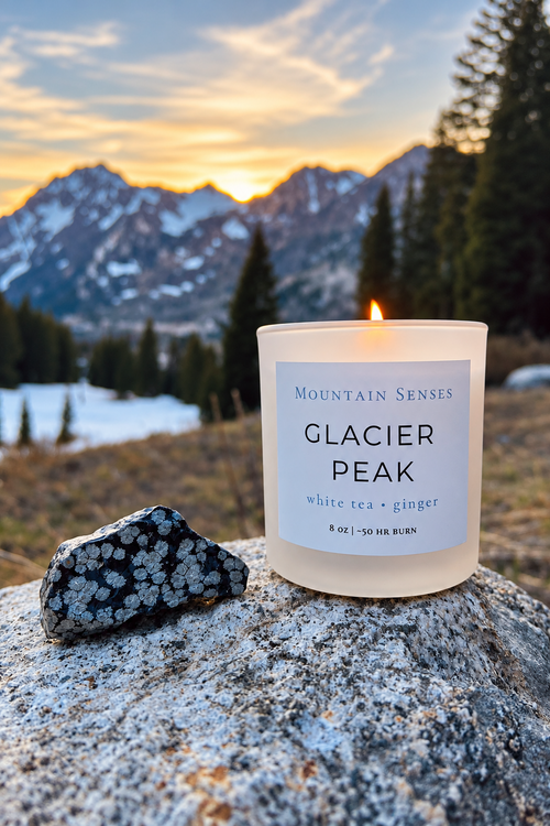 Glacier Peak candle styled with a seasonal stone against a snowy mountain landscape; stone not included
