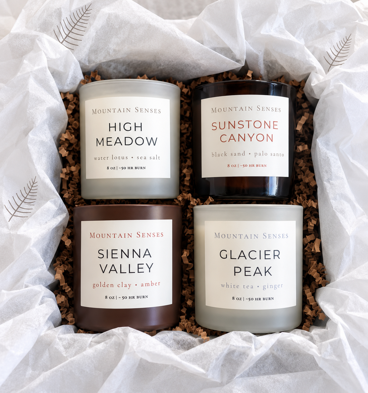 Four Seasons Candle Collection arranged in an open gift box with printed tissue paper and crinkle filler