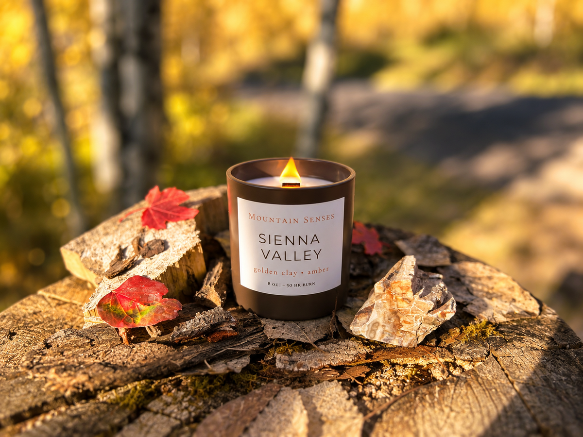 Lit Sienna Valley autumn candle with petrified wood and fall leaves in a wider golden aspen setting